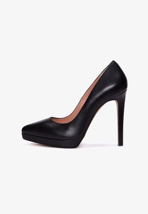 Sort læderpumpe med høj hæl og spids tå, platformsål og stiletthæl, vist fra siden på hvid baggrund.