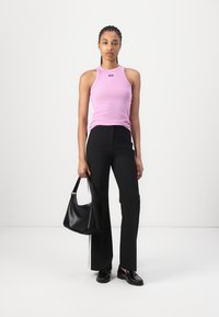Top a canotta senza maniche di colore rosa chiaro, pantaloni neri su misura e una borsa nera. La modella indossa scarpe nere, esposta su uno sfondo bianco.