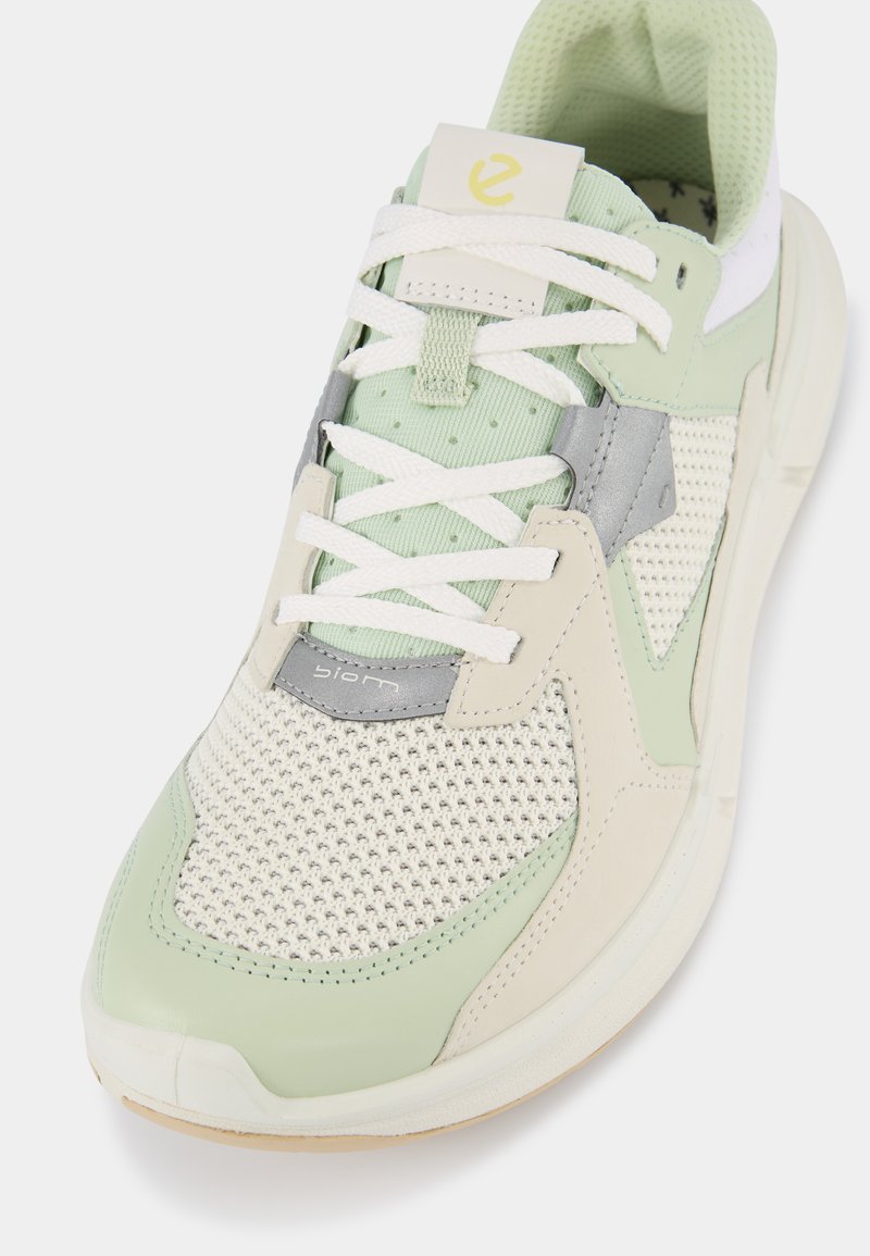 Hellgrüner Sportschuh mit Obermaterial aus Netzgewebe, Wildlederakzenten, weißen Schnürsenkeln und einer strukturierten Gummisohle. Besitzt ein Logo auf der Zunge.