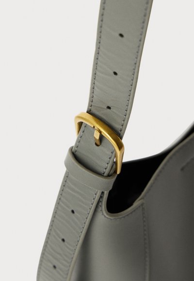 Cinghia per borsa a tracolla in pelle grigia con una fibbia in metallo dorato. Presenta cuciture visibili e lunghezza regolabile con più fori.