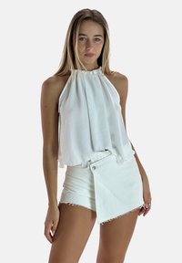 Haut blanc sans manches avec col halter froncé, associé à un short blanc taille haute avec un design enveloppant et un ourlet effiloché.