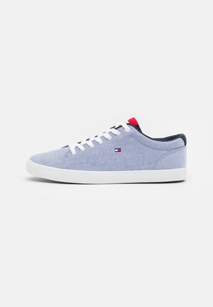Zapatilla deportiva de color azul claro con cordones blancos, suela blanca, pequeño logo rojo, blanco y azul en el lateral y detalles rojos y azul marino en la lengüeta y el talón.