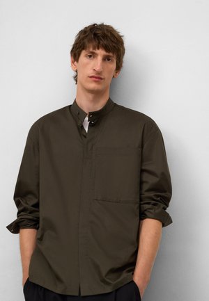 Dark green shirt with a high collar, buttoned front, and single chest pocket. Long sleeves are rolled up at the wrists. Smooth fabric texture.