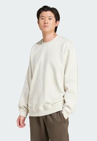 Cream sweatshirt with ribbed crew neck and cuffs, featuring a subtle logo on the chest. Paired with dark brown sweatpants.