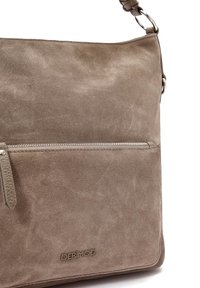 Miękka torba listonoszka z zamszu w kolorze taupe, z kieszenią na zamek i teksturowanym paskiem. Logo tłoczone z przodu. Gładkie wykończenie, minimalistyczny design.