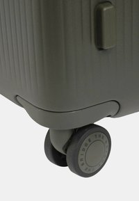 Valigia rigida di colore verde oliva con righe verticali, dotata di una maniglia robusta e di ruote nere a scorrimento fluido con dettagli di marca.