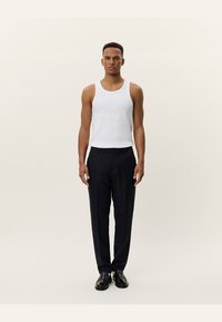White cotton tank top paired with dark navy tailored trousers, featuring a straight cut and a smooth fabric texture. Black shoes complete the outfit.