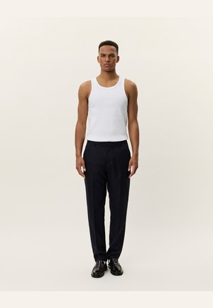 White cotton tank top paired with dark navy tailored trousers, featuring a straight cut and a smooth fabric texture. Black shoes complete the outfit.