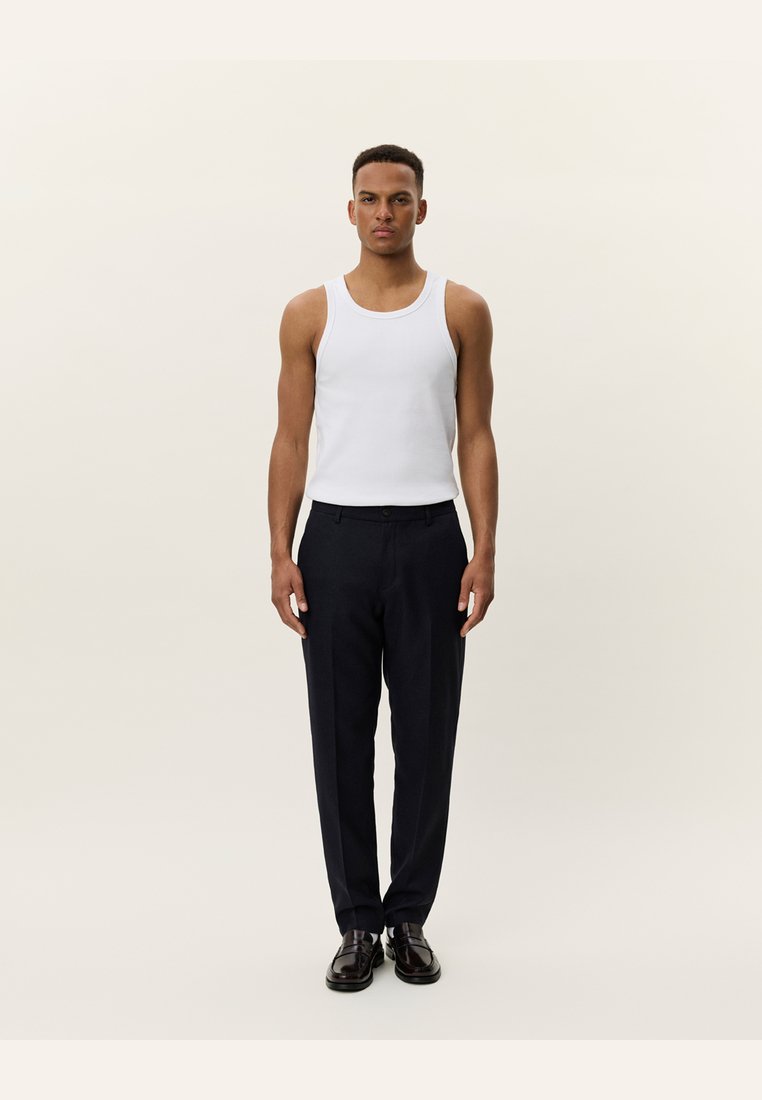 White cotton tank top paired with dark navy tailored trousers, featuring a straight cut and a smooth fabric texture. Black shoes complete the outfit.