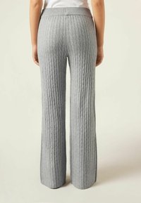 Pantalones de punto grises con una textura acanalada, que presentan un diseño de pierna ancha y una cintura elástica. Las costuras visibles realzan el patrón general.