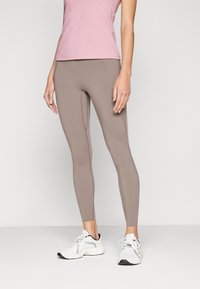 Lys rosa treningsgenser kombinert med stramme, brune leggings. Leggingsene har subtile sømdetaljer og smalner mot anklene. Hvite joggesko.