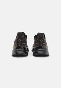 Black athletic shoes with a textured mesh upper, glossy accents, and a padded collar. Features elastic straps for secure fit and traction sole.
