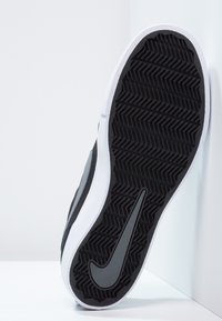 Mustat ja harmaat lenkkarit, joissa on teksturoitu kumipohja kalanruotokuvioinnilla, valkoinen välipohja ja Nike-logomerkki sivussa.