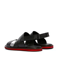 Zwarte leren sandalen met meerdere banden, open achterkant en een rode accenten op de zool. Beschikt over een platte, gematteerde basis voor comfort.