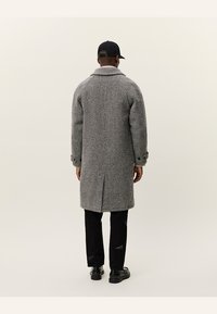 Grijs visgraat wollen jas met een notch-kraag, lange mouwen en een achterventilatie. Bevat zwarte knoopaccenten en heeft een getailleerde pasvorm.