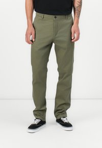 Olive green, straight-leg pants made of sturdy fabric, featuring a button closure, belt loops, and side pockets. Paired with black sneakers.
