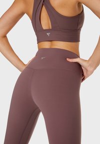 Mauve sportbeha met een cross-back ontwerp en bijpassende high-waisted leggings. Beide hebben naadloze accenten en een getailleerde silhouet.