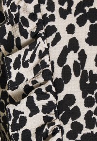 Leopardmönstrad tyg i beige med svarta fläckar och vågiga kanter, med en strukturerad väv för extra detalj.