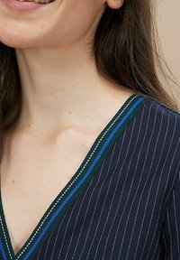 Navy-Bluse mit V-Ausschnitt, verziert mit vertikalen weißen Streifen und einem mehrfarbigen Besatz in Grün, Blau und Weiß um den Halsauschnitt.