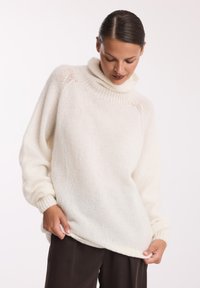 Biały, oversize'owy sweter z golfem wykonany z miękkiego, teksturowanego materiału, z prążkowanymi mankietami i dołem, w połączeniu z ciemnymi, luźnymi spodniami.