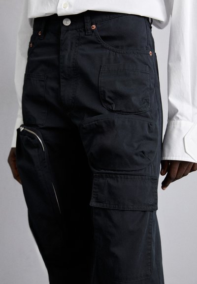 Black cargo pants featuring multiple pockets, a zippered side pocket, and a smooth, matte texture. Pairing with a white shirt.