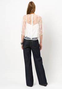 Durchsichtige weiße Bluse mit floralem Stickerei, kurzen Ärmeln und lockerer Passform, kombiniert mit dunklen, weit geschnittenen Denim-Jeans.