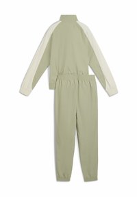 Tweedelig trainingspak in lichtgroen met crème accenten; voorzien van een hoge kraag en elastische taillebanden. Gemaakt van glad, lichtgewicht materiaal.