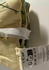 Sæt af fire bløde stofpuder i nuancer af beige, grøn og blå med mønstre af blade og insekter. Hvidt mærke med snore indeholder vaskeanvisninger.