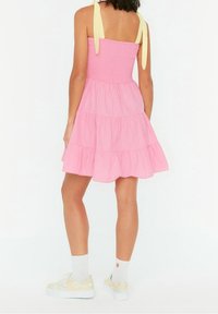 Rosa gestufte Sommerkleid mit gemustertem Oberteil und gelben Bindebändern. Kombiniert mit weißen Socken und gemusterten Sneakers, die einen lässigen und entspannten Look präsentieren.