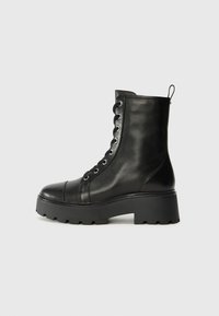 Bottines noires en cuir avec un bout rond, semelle en caoutchouc chunky et œillets en métal. Présente un design à lacets et une languette à l'arrière.