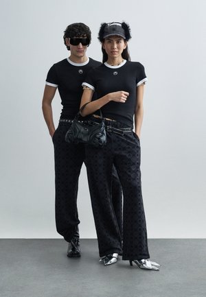 Svarta figurnära t-shirts med vita kanter, mönstrade svarta vida byxor, svart handväska, silverdetaljer och blanka spetsiga skor.