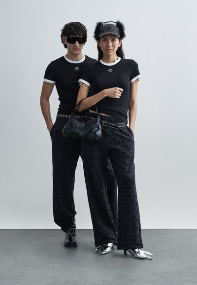 Μαύρα εφαρμοστά μπλουζάκια με λευκή επένδυση, μαύρο παντελόνι φαρδύ με σχέδια, μαύρη τσάντα, ασημένιες λεπτομέρειες και λαμπερά μυτερά παπούτσια.