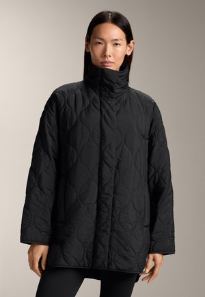 Zwarte gewatteerde jas met hoge kraag, met een gladde textuur en afgeronde, gestikte patronen. Geknipt in een oversized silhouet.