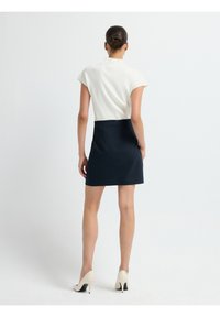 Vit ribbad kortärmad topp kombinerad med en figursydd marinblå kjol. Modellen bär krämfärgade klackskor. Släta ytor och enkel design.