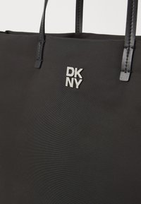 Fekete tote táska texturált nylonból, lapos szintetikus pántokkal. Az elején ezüst színű DKNY logó található. Egyszerű és funkcionális design.