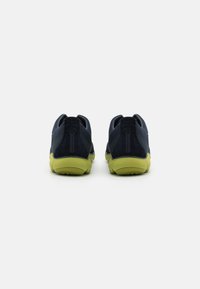 Scarpe sportive blu navy con materiale testurizzato e suole verdi, caratterizzate da un design minimalista e una linguetta sul tallone.