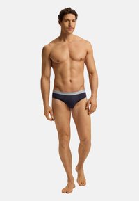 Herren-Bikini in Marineblau aus weichem Stoff mit einem grauen Bund, auf dem der Markenname geprägt ist. Figurbetontes Design, flache Nähte für hohen Tragekomfort.