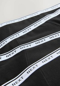 Black fabric featuring horizontal white bands with the word "NEXT" in black. The design includes a textured finish and visible stitching.