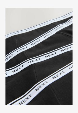 Zwart textiel met witte banden waarop "NEXT" in het zwart is gedrukt. De stof oogt glad en heeft een gestikt geometrisch patroon.