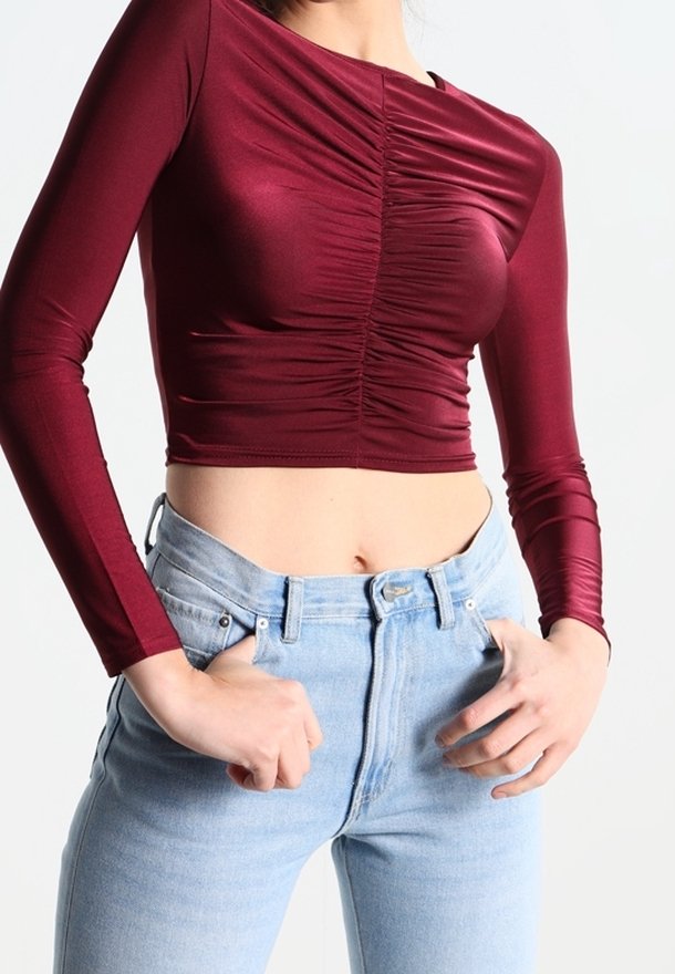 Burgundské dlouhé rukávy crop top s nařasenými detaily, spárovaný s vysokými modrými džíny. Hladká, přiléhavá látka s jemným leskem.