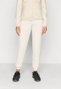 Φωτεινό μπεζ μπουφάν με φερμουάρ και υφασμένα μανίκια, συνδυασμένο με κρεμ παντελόνι jogger και μαύρα αθλητικά παπούτσια από δίχτυ. Απλή και λειτουργ�ική αθλητική ενδυμασία.