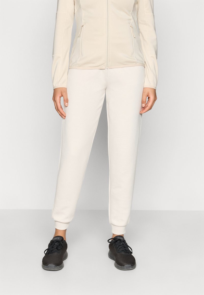 Φωτεινό μπεζ μπουφάν με φερμουάρ και υφασμένα μανίκια, συνδυασμένο με κρεμ παντελόνι jogger και μαύρα αθλητικά παπούτσια από δίχτυ. Απλή και λειτουργική αθλητική ενδυμασία.