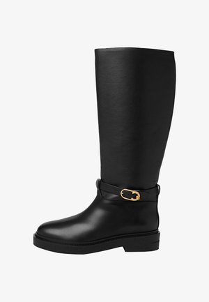 Bota de cuero negra hasta la rodilla con una textura suave, punta redondeada y un acento de hebilla dorada en la correa. Suela gruesa para mayor estabilidad.