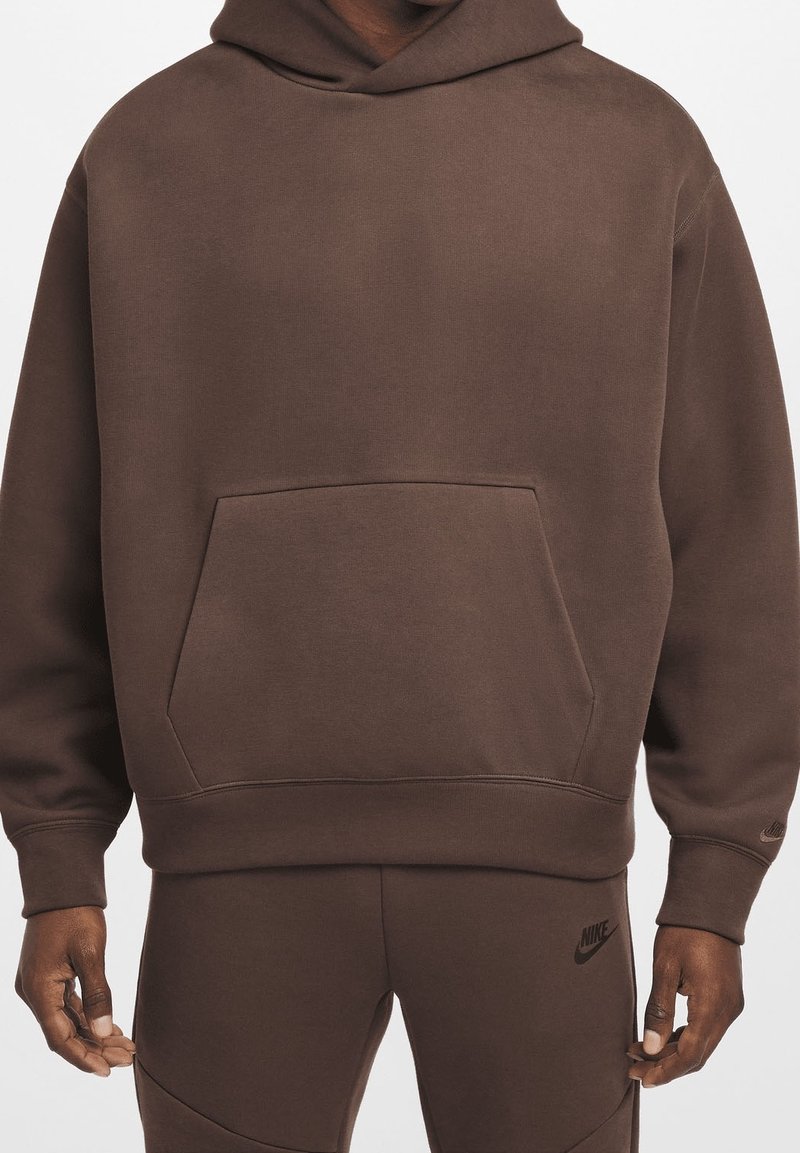 Haut à capuche marron en tissu doux, doté d'une poche kangourou à l'avant, de poignets côtelés et d'une capuche avec cordon de serrage. Le logo Nike est visible à l'avant.