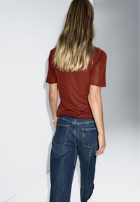 Rust-colored short-sleeve t-shirt paired with loose blue denim jeans featuring a classic five-pocket design and faded wash.