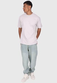 Jasnoszary bawełniany t-shirt z krótkim rękawem, połączony z jasnoniebieskimi luźnymi dżinsami i białymi trampkami. Model stoi z rękami w kieszeniach.