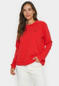 Rotes Sweatshirt mit rundem Ausschnitt, langen Ärmeln und einem Saum. Hat eine kleine schwarze "love"-Stickerei auf der Brust. Glatte Textur.