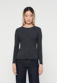 Pull long gris foncé à manches longues avec un col rond, texture côtelée et ourlet à peplum, associé à un jean foncé. Design minimaliste.