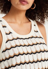 Stickad linne med krämfärgad tyg och svarta och bruna zigzag-mönster, ribbad textur och rund halsringning.