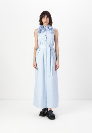 Robe maxi sans manches bleu clair avec un devant à boutons et une ceinture. Détails floraux remarquables au col. Portée avec des chaussures noires épaisses.